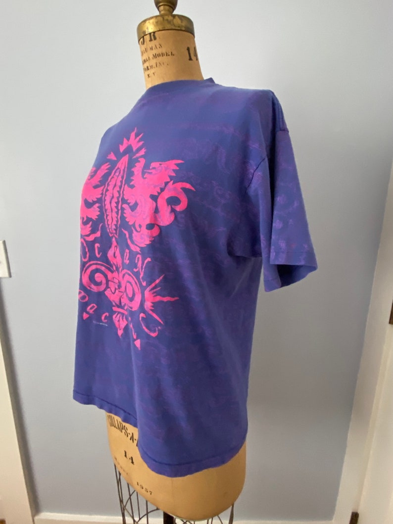 May include: A purple t-shirt with a pink graphic of a stylized design with the word "Ocean" in the center.