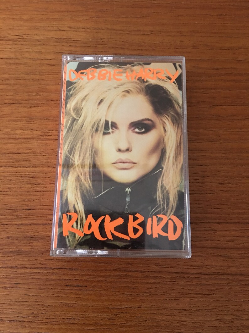 May include: A cassette tape with a clear plastic case. The front of the tape features a photo of Debbie Harry, the lead singer of Blondie, with the title "Rockbird" in orange text.