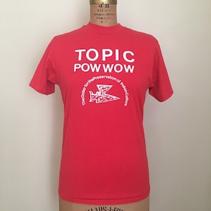 Puede incluir: Camiseta roja con texto blanco que dice "TOPIC POW WOW" y un logotipo blanco que dice "The Order for the Preservation of Indian Culture".