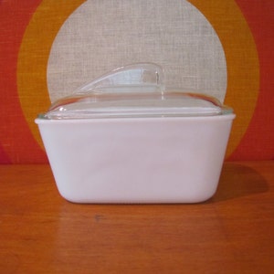 Puede incluir: Plato para hornear rectangular de vidrio blanco con una tapa de vidrio transparente. La tapa tiene un asa en la parte superior.