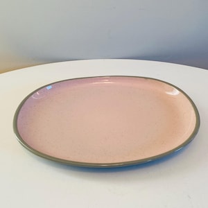 Op de afbeelding: Een lichtroze ovale serveerschaal met een gespikkelde afwerking en een donkergrijze rand.