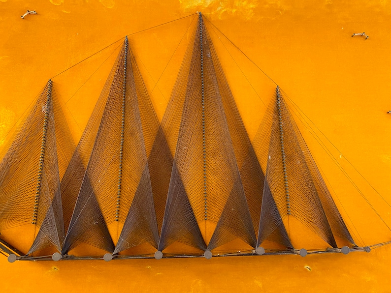 May include: A wall hanging made of string stretched between nails, forming a geometric pattern of triangles. The string is a dark brown color, and the nails are silver. The background is a bright yellow.