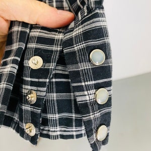 May include: Close-up of a black and white plaid shirt cuff with four pearly white buttons.