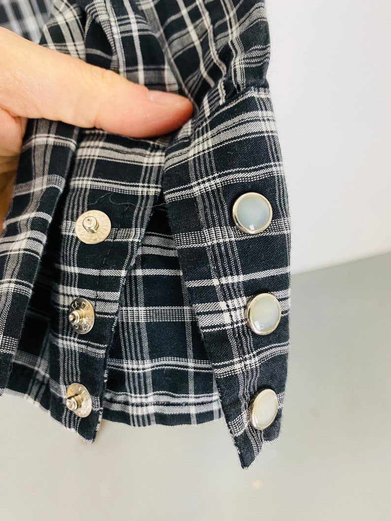 May include: Close-up of a black and white plaid shirt cuff with four pearly white buttons.