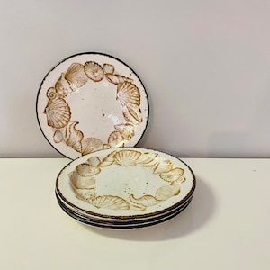 Op de afbeelding: Set van vier witte keramische borden met een bruin schelpmotief. De borden hebben een donkerbruine rand.