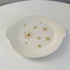 Op de afbeelding: Witte keramische serveerschaal met twee handvatten en een gouden sneeuwvlokkenontwerp.