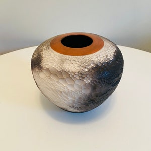 Könnte beinhalten: Eine strukturierte Keramikvase mit runder Form und breiter Öffnung. Die Vase weist einen Farbverlauf von Schwarz zu Weiß auf, mit einem braunen Rand. Die Oberfläche hat ein einzigartiges, schuppenartiges Muster.