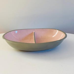 Op de afbeelding: Een verdeelde serveerschaal met een lichtroze binnenkant en een grijze buitenkant. De schaal is ovaalvormig en heeft een gladde, glanzende afwerking.