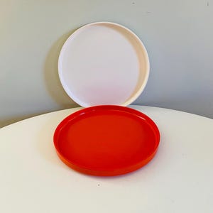 Może przedstawiać: Dwa okrągłe talerze, jeden biały, a drugi czerwony, ułożone jeden na drugim.