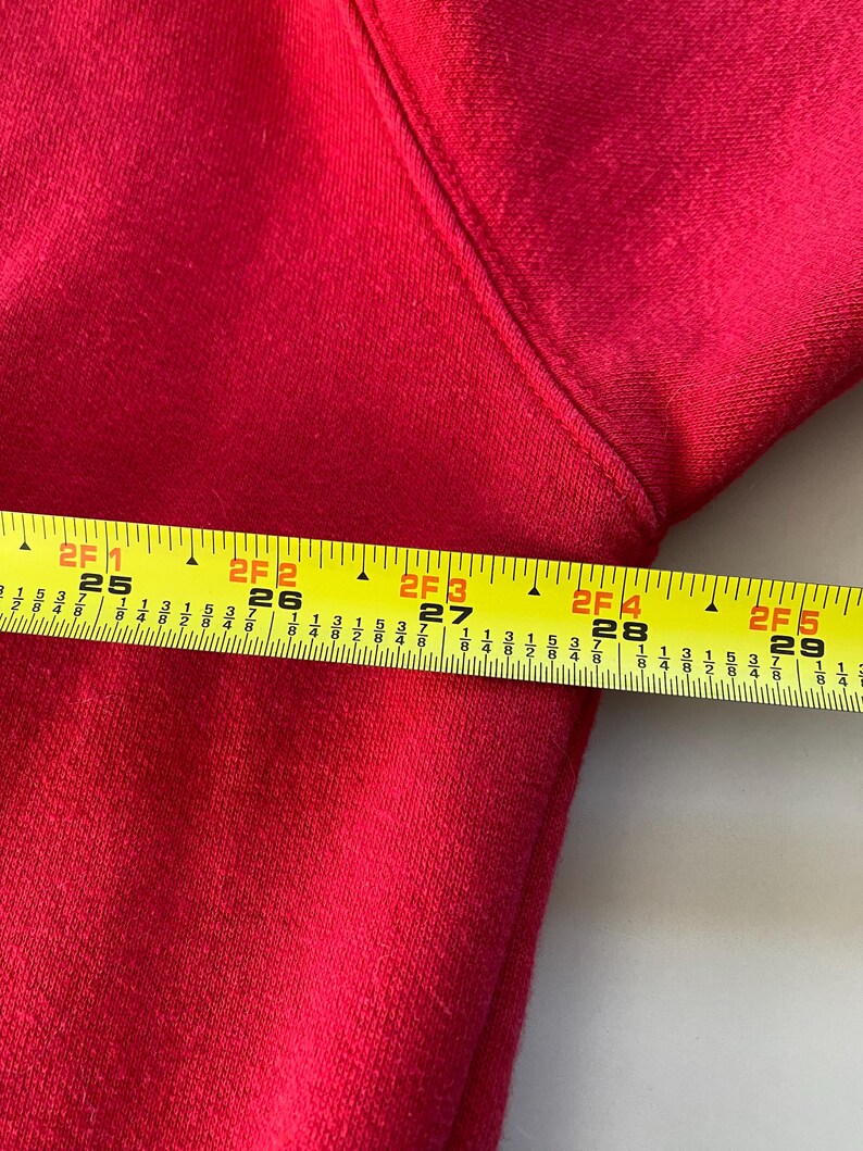 May include: Close-up of a red fabric with a yellow measuring tape. The tape reads "2F 1 25" to "2F 5 29".