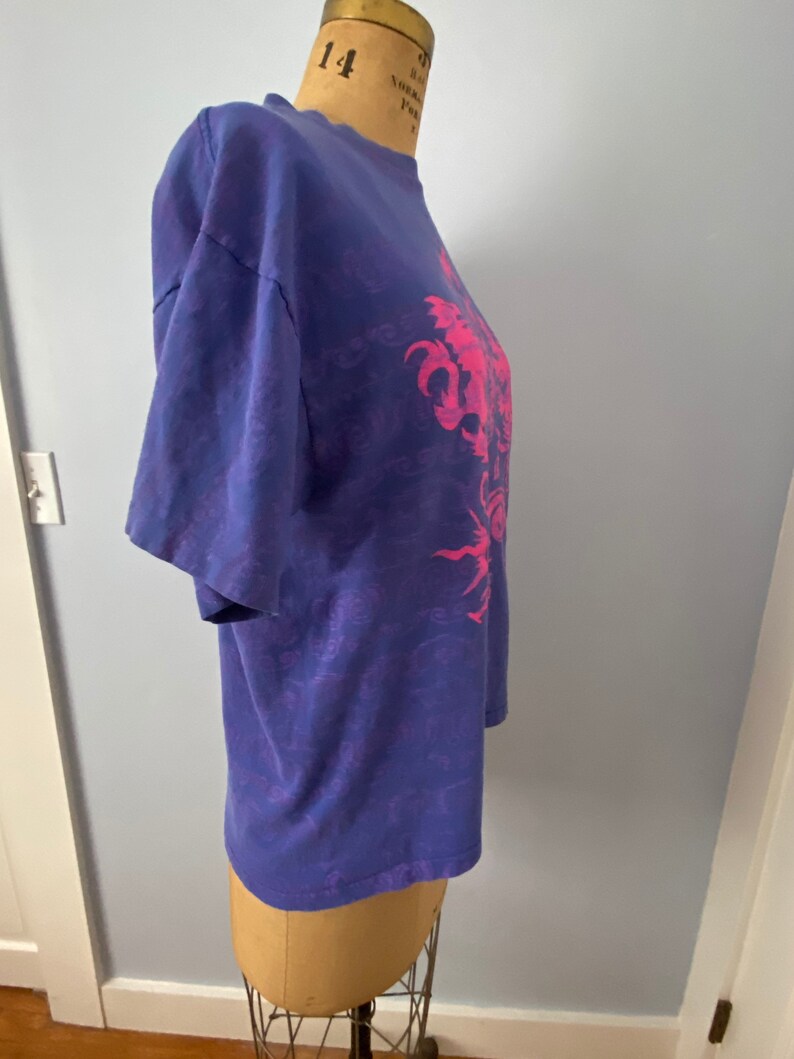 May include: A purple tie-dye t-shirt with a pink graphic of a dragon. The dragon is surrounded by a swirling pattern.