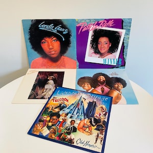 May include: Four vinyl records with album covers featuring singers Linda Lewis, Pattie LaBelle, and the group The Message. The Linda Lewis album cover features a photo of the singer with a blue background. The Pattie LaBelle album cover features a photo of the singer with a purple background. The Message album cover features a photo of the group with a blue background. The fourth album cover features a colorful illustration of a city skyline with the text "Listen to the Message" and "Freedom" on the cover.