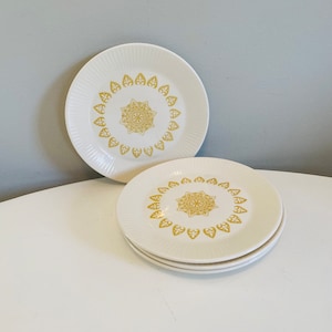 Op de afbeelding: Set van vier witte keramische dessertborden met een gouden bloemenontwerp. De borden hebben een gegolfde rand en een verhoogd midden.