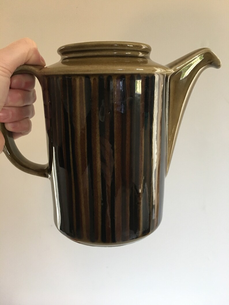 Puede incluir: Una cafetera de cer&aacute;mica rayada en marr&oacute;n y negro con asa y pico.