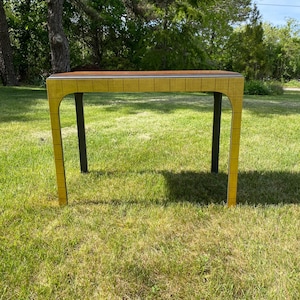 May include: A yellow table with a rectangular top and curved legs. The table has a brown top and dark gray legs. The table is set on a grassy lawn.