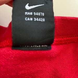 May include: Black and white Nike tag with the text "RN# 94878 CA# 34428" on a red shirt.