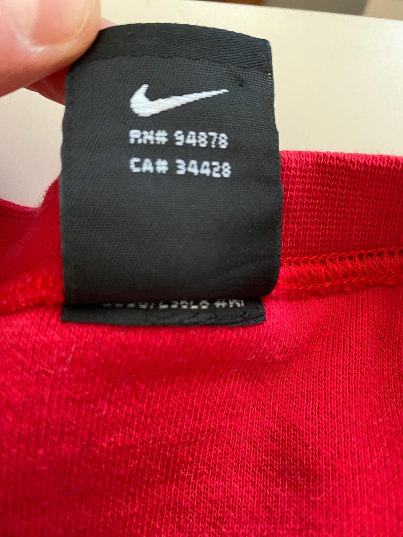 May include: Black and white Nike tag with the text "RN# 94878 CA# 34428" on a red shirt.