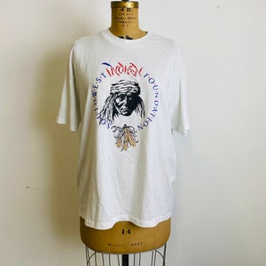 Puede incluir: Camiseta blanca con un gráfico de la cara de un hombre nativo americano con el texto "Southwest Indian Foundation" alrededor de la imagen.
