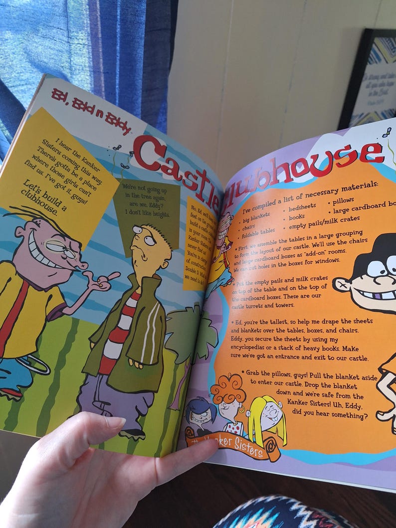 May include: Open book with colorful illustrations from "Ed, Edd n Eddy." The page features cartoon characters and text, including "Castle Clubhouse" in large letters. The text describes how to build a clubhouse.