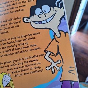 May include: A page from a children's book featuring a cartoon character with black hair, a large grin, and an orange shirt. The character is positioned on the right side of the page. Text is visible on the page, with the number 21 in the bottom right corner.