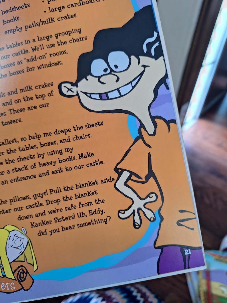 May include: A page from a children's book featuring a cartoon character with black hair, a large grin, and an orange shirt. The character is positioned on the right side of the page. Text is visible on the page, with the number 21 in the bottom right corner.
