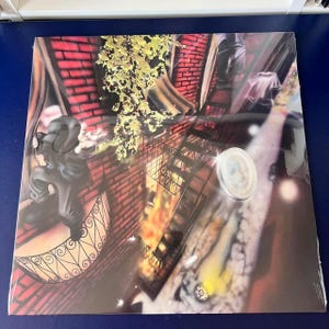 Op de afbeelding: Een kleurrijk, abstract schilderij dat een stadsscène afbeeldt met een persoon in zwarte kleding die van een gebouw springt. Het schilderij heeft een levendige, bijna psychedelische stijl met een mix van rode, gele, oranje en blauwe kleuren.