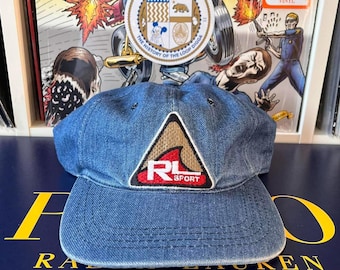 以下が含まれることがあります： 赤と白の「RL SPORT」の文字と波が描かれた三角形のワッペンが付いた、青いデニムのベースボールキャップです。