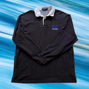 Puede incluir: Camiseta de rugby negra de manga larga con cuello blanco y un logotipo azul de Polo Sport en el pecho.