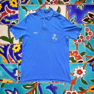 May include: A blue polo shirt with a white embroidered logo on the left chest pocket. The logo says "Polo" and "RL-83".