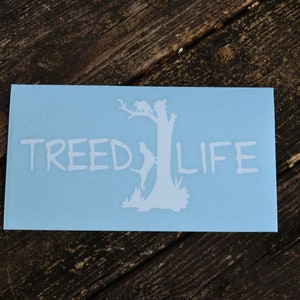 May include: A light blue sticker with a white silhouette of a tree with a raccoon climbing it. The text "TREED LIFE" is written in white below the tree.