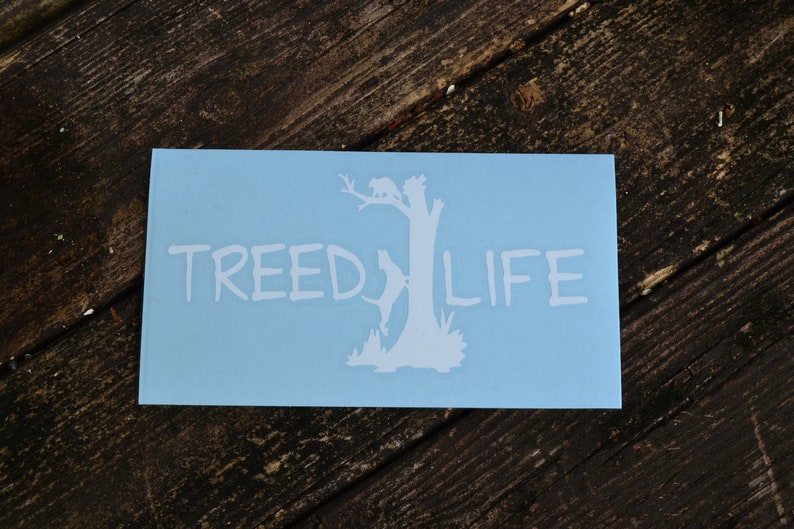 May include: A light blue sticker with a white silhouette of a tree with a raccoon climbing it. The text "TREED LIFE" is written in white below the tree.