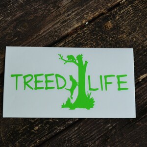 May include: A white sticker with a green silhouette of a tree with a bird and a dog on it. The text "TREE LIFE" is written in green below the tree.