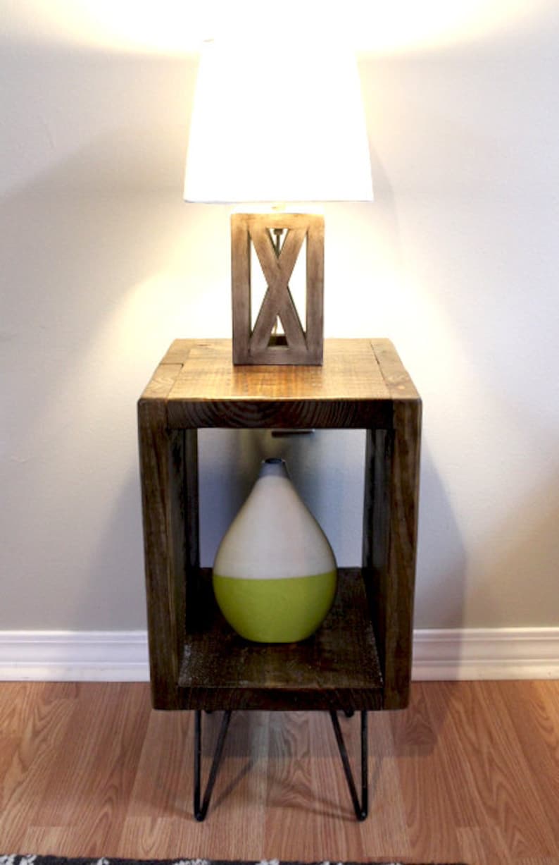 May include: A wooden end table with a white lampshade and a green and white ceramic vase. The table has a square top and three hairpin legs.