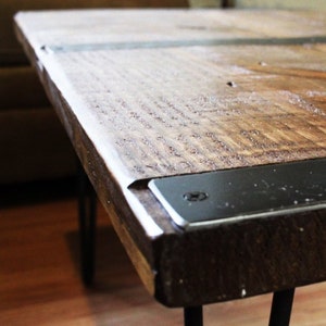 May include: A wooden coffee table with a dark brown finish and black metal accents. The table has a rustic look and is supported by hairpin legs.