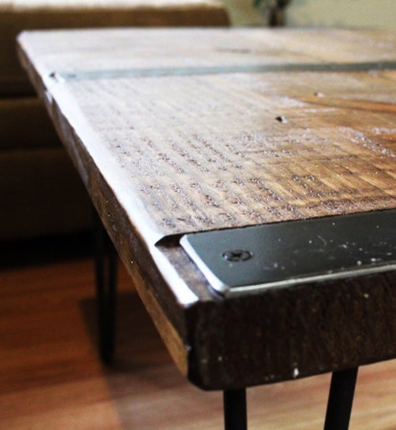May include: A wooden coffee table with a dark brown finish and black metal accents. The table has a rustic look and is supported by hairpin legs.
