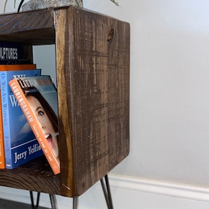 May include: A dark brown wooden end table with a shelf and hairpin legs. The table has a small potted plant on top and a stack of books on the shelf. The books include "Of War and Weddings" and "Talking as Fast as I Can" by Lauren Graham.