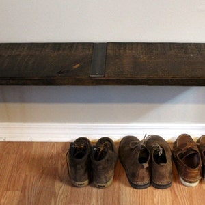 May include: A dark brown wooden bench with black metal hairpin legs. The bench is sitting on a wooden floor and has a pair of brown leather shoes underneath.