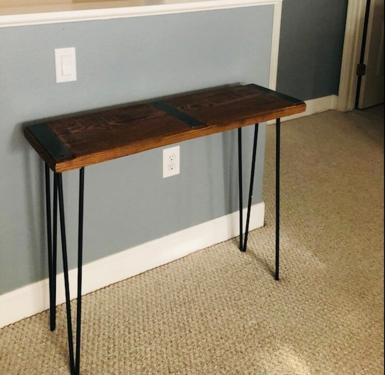 May include: A dark brown wooden console table with black metal hairpin legs. The table has a rustic, industrial style.