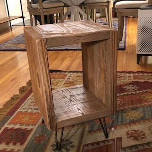 May include: A rustic wooden end table with a single shelf and hairpin legs. The table is made of reclaimed wood and has a natural, weathered finish.