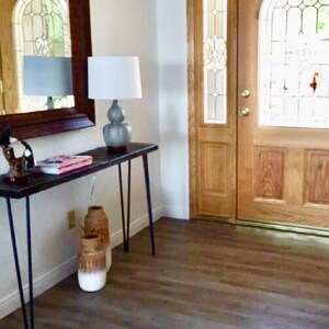 May include: A wooden entryway with a brown door with glass panels and a white lamp on a black table with three vases.