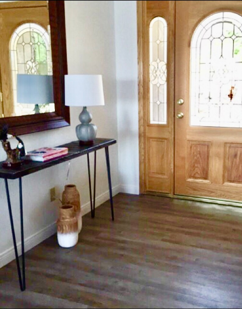 May include: A wooden entryway with a brown door with glass panels and a white lamp on a black table with three vases.
