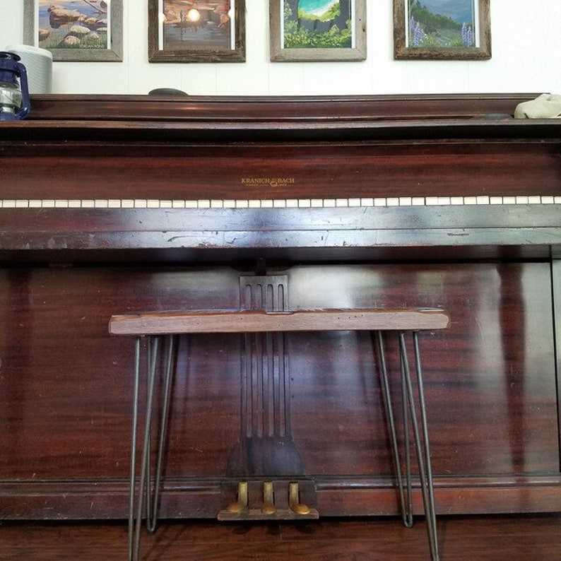 May include: A vintage upright piano with a dark wood finish and a black metal stool with hairpin legs. The piano has a white keyboard and the name "Kranich & Bach" is visible on the front.