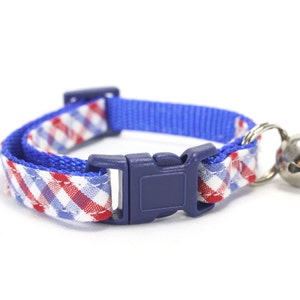 Puede incluir: Un collar de gato a cuadros azules y blancos con una hebilla ajustable azul y una campanilla plateada.