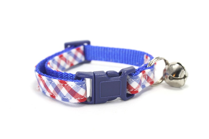 Puede incluir: Un collar de gato a cuadros azules y blancos con una hebilla ajustable azul y una campanilla plateada.