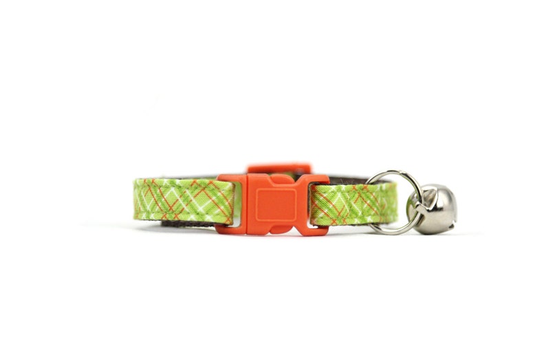 May include: A green and orange plaid cat collar with an orange plastic buckle and a silver bell.