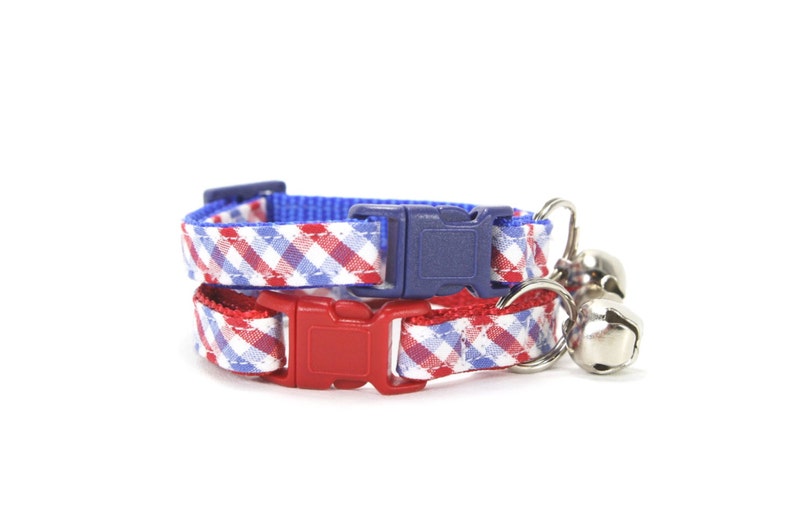 Puede incluir: Un collar para gato de cuadros rojos y azules con una campanilla. El collar tiene un cierre de hebilla de pl&aacute;stico.