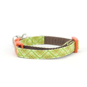 Puede incluir: Un collar para perro de tela a cuadros verde y naranja con una correa marr&oacute;n y hebillas de pl&aacute;stico naranja.