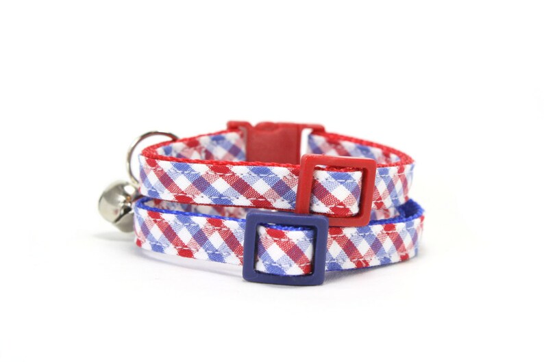 Puede incluir: Dos collares de gato de cuadros rojos y azules con hebillas de pl&aacute;stico ajustables. Los collares est&aacute;n superpuestos.