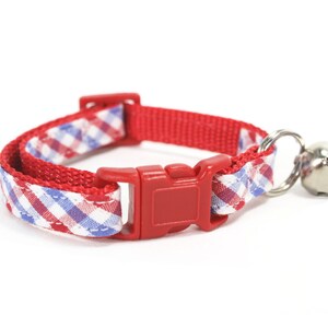 Puede incluir: Collar de gato rojo y azul a cuadros con una hebilla de pl&aacute;stico roja y una campana plateada.