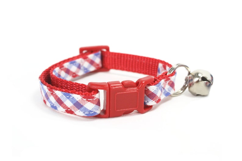 Puede incluir: Collar de gato rojo y azul a cuadros con una hebilla de pl&aacute;stico roja y una campana plateada.